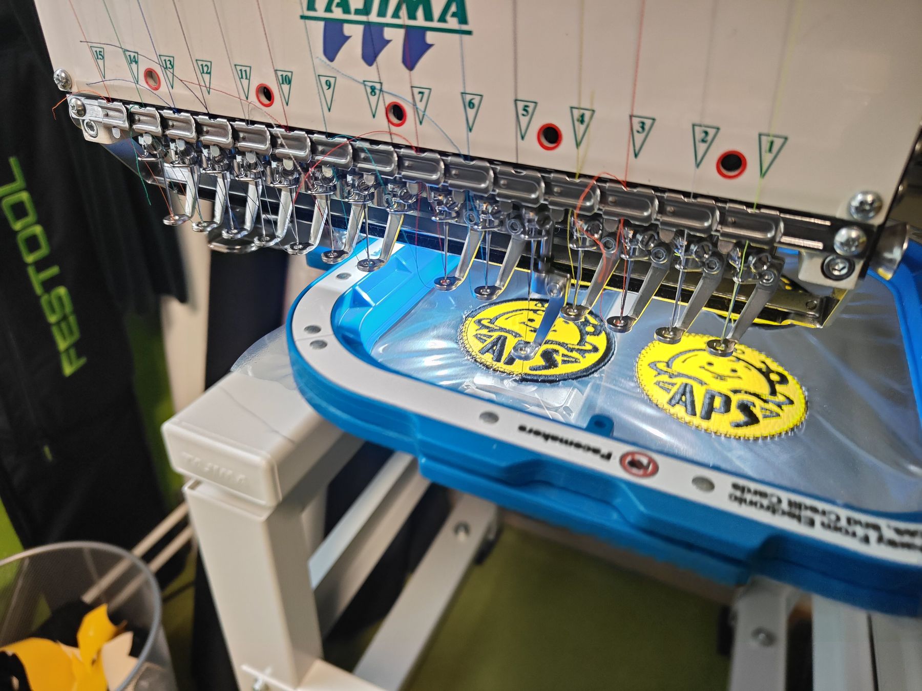 Borduurmachine borduurt gele APS-emblemen op donkere stof in het atelier in Haarlem Borduurmachine borduurt gele APS-emblemen op donkere stof in het atelier in Haarlem