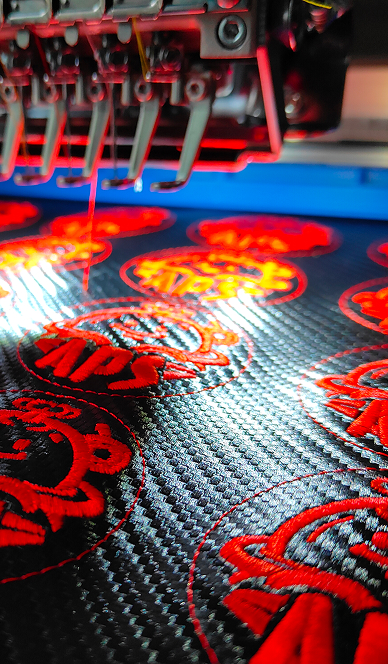 Close-up van rode geborduurde emblemen op carbonlook-stof in de borduurmachine Close-up van rode geborduurde emblemen op carbonlook-stof in de borduurmachine